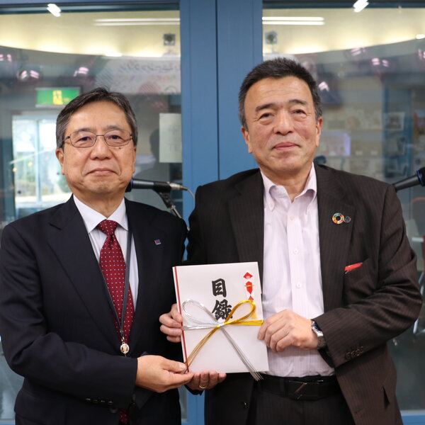 ラジオ出演し募金の目録を渡す佐久間常務（右）