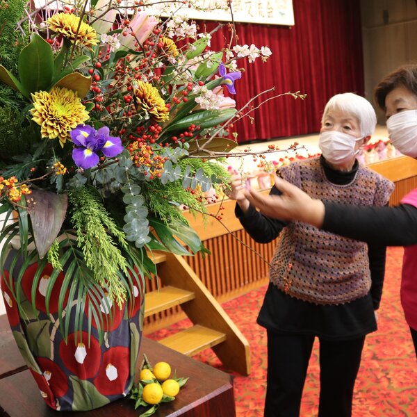 同地区女性部事務局長の佐藤惠子さんが手がけた生け花を見る部員たち
